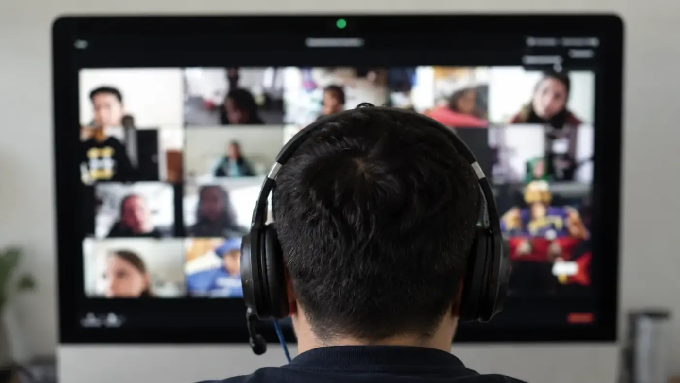 Alumno con audífonos siguiendo una clase en vivo por videollamada, con el resto del grupo en pantalla